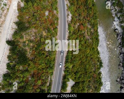 Aerial drone view of rocky canyon Moraca river with big stone boulders, asphalt road with moving cars, Montenegro. Vibrant lush green vegetation in su Stock Photo