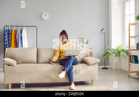 Young african american business woman working with laptop computer at home sitting on sofa. Stock Photo