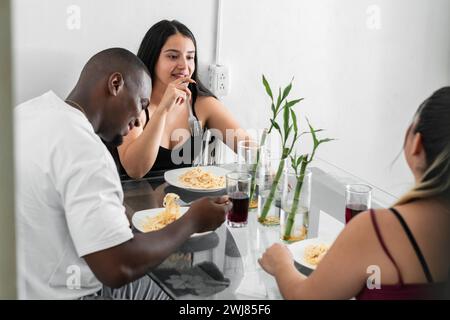 three latin friends, gathered together having lunch, spending their free time together, while smiling and chatting. Stock Photo