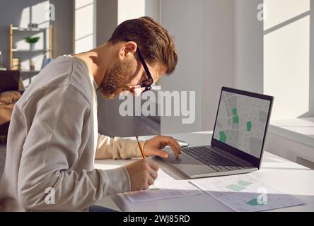 Professional cartographer working with printed cadastral map at table on his workplace. Stock Photo