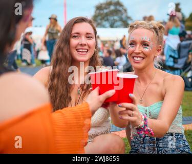 Three Female Friends Wearing Glitter Having Fun At Summer Music Festival Doing Cheers With Drinks Stock Photo