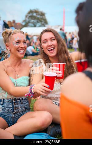 Three Female Friends Wearing Glitter Having Fun At Summer Music Festival Doing Cheers With Drinks Stock Photo