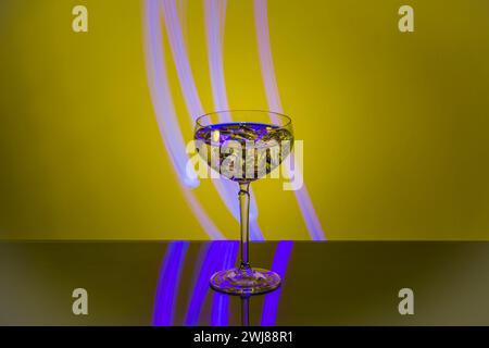Close-up of martini glass with ice isolated on yellow-purple abstract backdrop. Stock Photo
