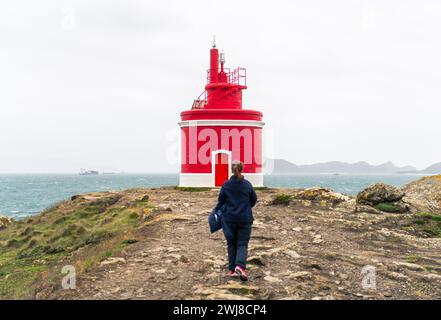 Woman hiking on the cliffs near a red lighthouse Stock Photo