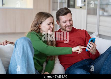 Loving couple sitting on sofa, looking photos, videos in internet, spending pastime together at home Stock Photo