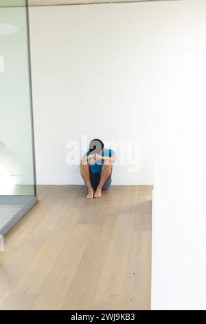 Teenage Asian boy sits alone on a wooden floor, with copy space Stock Photo