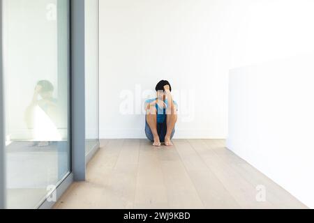 Sad teenage Asian boy sits alone on a wooden floor, with copy space Stock Photo