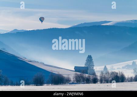 A hot air balloon floating over snow-covered mountains and valleys Stock Photo
