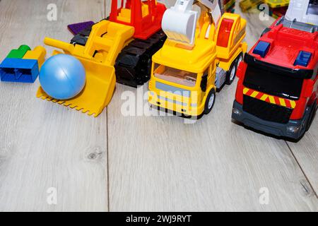 children's toy cars made of plastic, a fire truck, an excavator, a tractor, are on the floor Stock Photo