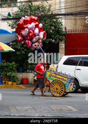 Manila, Manila, The Philippines. 14th Feb, 2024. A ice-cream vendor with helium balloons in the shape of a heart walks in a neighbourhood on Valentine's Day. Local media say the festival is expected bring economic benefits to the country as people spend more money on buying flowers, chocolates and other gifts to show their commitment and love for their partners. (Credit Image: © Daniel Ceng Shou-Yi/ZUMA Press Wire) EDITORIAL USAGE ONLY! Not for Commercial USAGE! Stock Photo