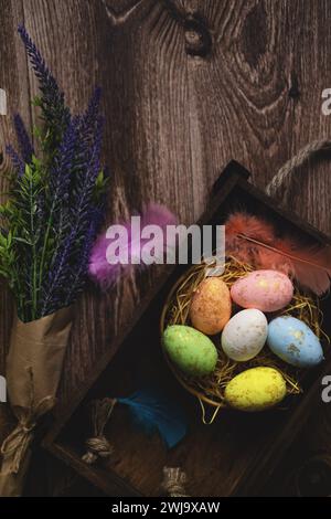 Flat lay composition of colourful painted easter eggs in a hay basket on wooden table. Happy Easter celebration Stock Photo