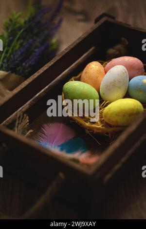 Flat lay composition of colourful painted easter eggs in a hay basket on wooden table. Happy Easter celebration Stock Photo