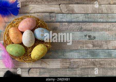 Flat lay composition of colourful painted easter eggs in a hay basket on wooden table. Happy Easter celebration Stock Photo