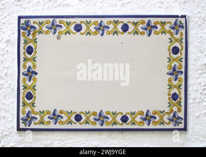 collage, spain house square pottery sign in enamel or clay on a rustic white wall. blue, yellow flowers, green leaves are drawn with yellow pattern Stock Photo