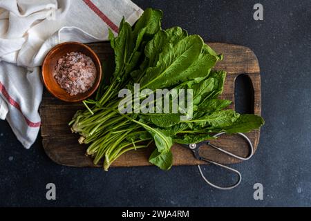 Top view of bunch of fresh arugula leaves alongside a bowl of pink salt and scissors on a rustic wooden cutting board, set against a dark tabletop wit Stock Photo