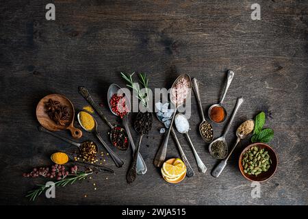 From above flat lay showcasing a variety of spices and seeds in spoons on a dark wooden surface, including sunflower seeds, anise stars, rosemary, min Stock Photo