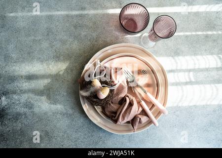 From above stylish Easter table setting featuring a nest with eggs, pastel tableware, and a delicate linen napkin. Stock Photo