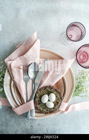 From above aesthetically pleasing Easter table arrangement featuring a nest with speckled eggs, nestled on stacked ceramic plates with a pink linen na Stock Photo