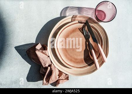 From above sophisticated Easter table setting featuring stacked ceramic plates, rose gold cutlery, and a linen napkin on a textured background. Stock Photo