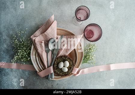Top view of an Easter table setting featuring a nest with eggs, surrounded by ceramic dishes, cutlery, and pastel linens. Stock Photo