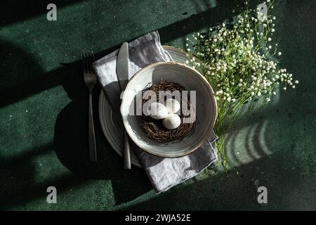 An elegant spring-themed table setting featuring a bird's nest with eggs, surrounded by delicate white flowers on a textured surface Stock Photo