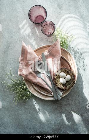 Top view elegant and simple table setting celebrates Easter with a bird's nest containing speckled eggs, surrounded by delicate china and soft pink li Stock Photo