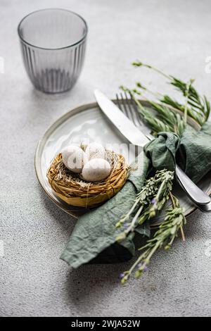 An elegant Easter table setting, featuring a small nest with speckled eggs on a ceramic plate, paired with a green napkin and lavender sprigs Stock Photo