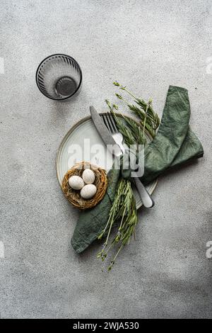 A top-view image featuring an elegant table setting with a rustic feel, including a linen napkin, ceramic plate, cutlery, a nest with eggs, and fresh Stock Photo