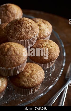 Close-up of golden-brown muffins arranged on a decorative glass serving plate, with a dark background. Stock Photo