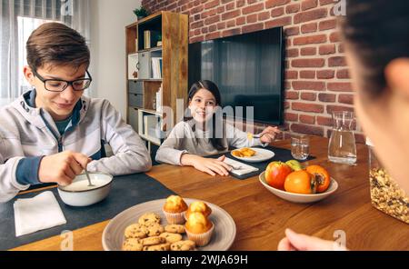 A family enjoys a weekend breakfast together at home with a spread of fruits, muffins, cookies, and cereal on the table Stock Photo