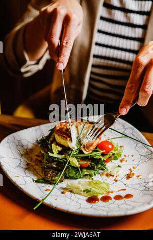 Close-up image a person cutting into a grilled chicken salad garnished with fresh greens and cherry tomatoes Stock Photo