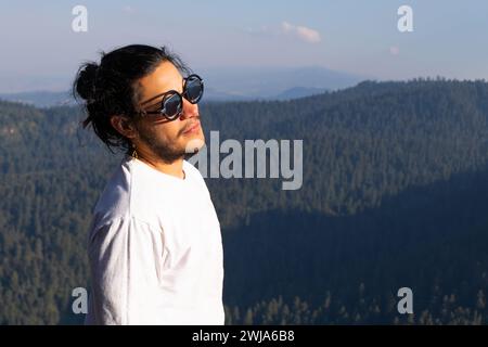 Side view of positive bearded guy in casual clothes and sunglasses looking away while enjoying nature during trip in Los Dinamos Stock Photo