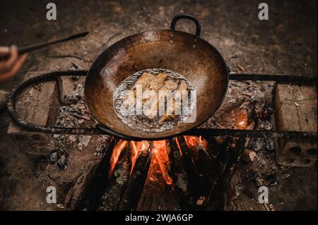 From above of hand with spatula frying homemade spring rolls with pan placed on fire in kitchen Stock Photo