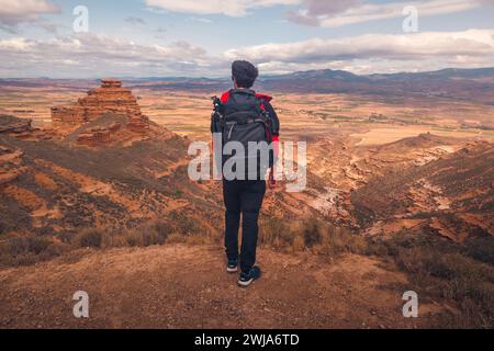 Back view of anonymous male tourist with backpack standing on hill and looking at picturesque landscape of Spanish badlands during sightseeing Stock Photo