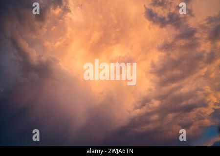 A breathtaking view of a dramatic sky filled with fiery orange and dim gray clouds at sunset, radiating intense light rays. Stock Photo