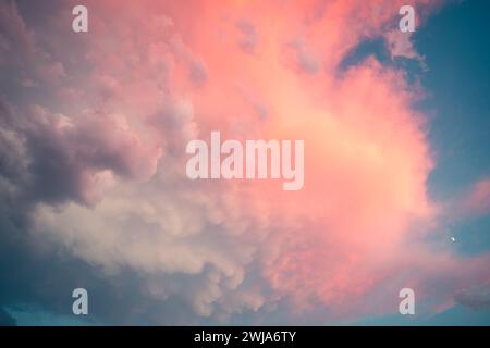 An enchanting sky captured at dusk, showcasing a palette of pink and blue hues with soft clouds and a distant crescent moon Stock Photo
