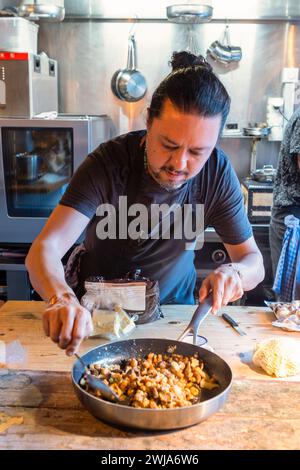 Concentrated chef wearing black apron making tasty Italian sausage in non sticky frying pan in restaurant at Zermatt Switzerland Stock Photo