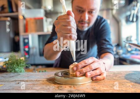 Crop focused chef using pastry bag to decorate tasty dessert on plate behind blurred kitchen background in restaurant at Zermatt Switzerland Stock Photo