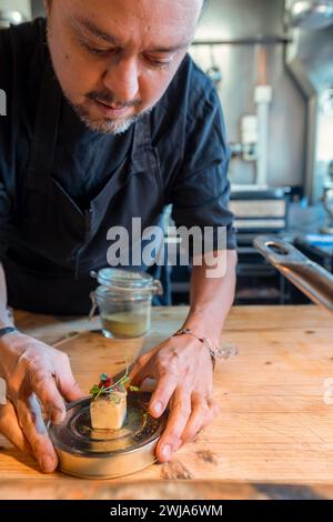 Young bearded chef wearing black shirt and apron with tasty cheese dessert and fresh green herb on top in restaurant at Zermatt Switzerland Stock Photo