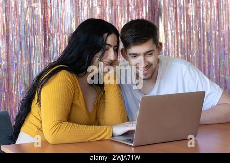 Happy bearded man sitting near smiling young woman using laptop and looking at screen in room Stock Photo