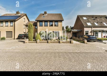 A sunny view of a quiet suburban street featuring modern detached and semi-detached houses with parked cars and lush greenery. Stock Photo