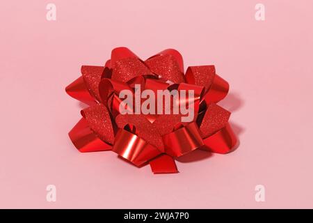 Glittering red bow on a smooth pink background, exemplifying a Valentine’s Day gift concept. Stock Photo