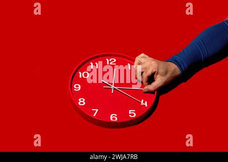 A person's hand is setting the time on a red wall clock with a striking red background, illustrating time management Stock Photo