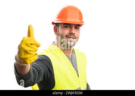 Trustworthy expression male builder in work equipment orange helmet yellow vest and gloves showing thumb-up like gesture with blank copyspace isolated Stock Photo