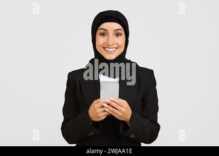Smiling Muslim businesswoman using smartphone, wearing hijab Stock Photo