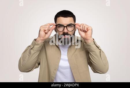 Serious smart millennial middle eastern man adjusting glasses, focused gaze, with thoughtful expression Stock Photo
