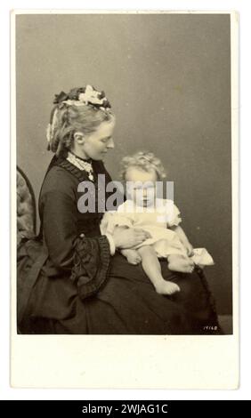 Original very clear, gorgeous, quality image of  Victorian CDV  Carte de Visite ( visiting card or CDV)  of a beautiful aristocartic Welsh woman, Victorian mother, with a cute child on her lap, wearomg a small cap with an elaborate haristyle. From the collection Arkwright Family Hampton Court Castle, Hereford  c. 1870 from exact hat and hair in La Mode Illustree dated 1870. Stock Photo