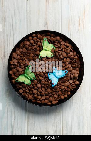 Chocolate drops for making chocolate and candies, sugar butterfly figures for decorating cakes on a light wooden background. Tempered chocolate Stock Photo