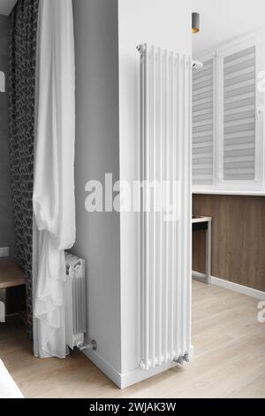 Modern designer vertical white heating radiator mounted on the wall in the interior of an apartment, house. A stylish solution for the design Stock Photo