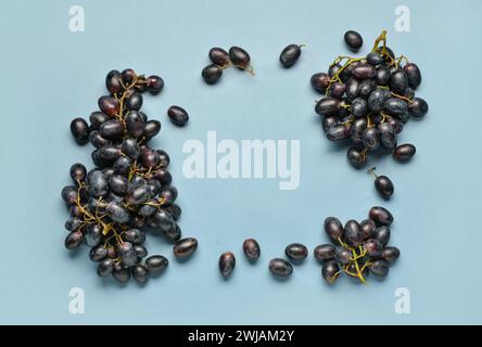 Frame made of sweet black grapes on blue background Stock Photo
